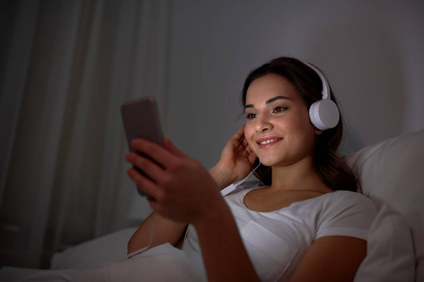 woman with smartphone and headphones in bed - Fotoğraf, Görsel