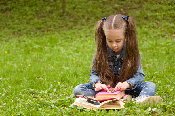 Little schoolgirl is reading a book in nature. Smart little pupi - Photo, Image