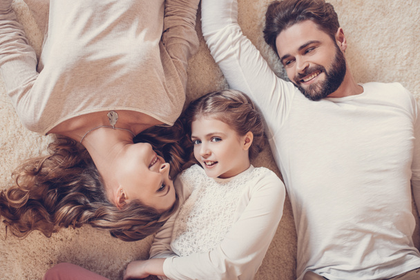 Top view of happy family with one child lying together on carpet - Фото, зображення