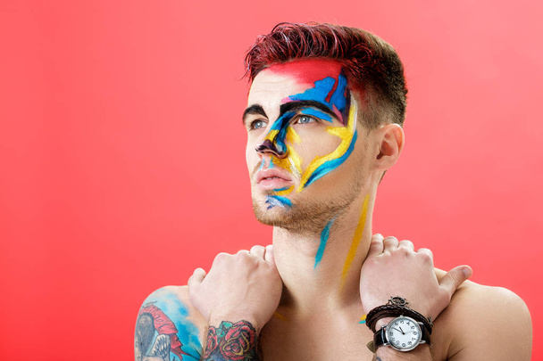 portrait of young man with colored face paint on red background. Professional Makeup Fashion. fantasy art makeup - Fotoğraf, Görsel