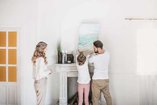 Happy family hanging picture of sea over the fireplace at home - Fotografie, Obrázek