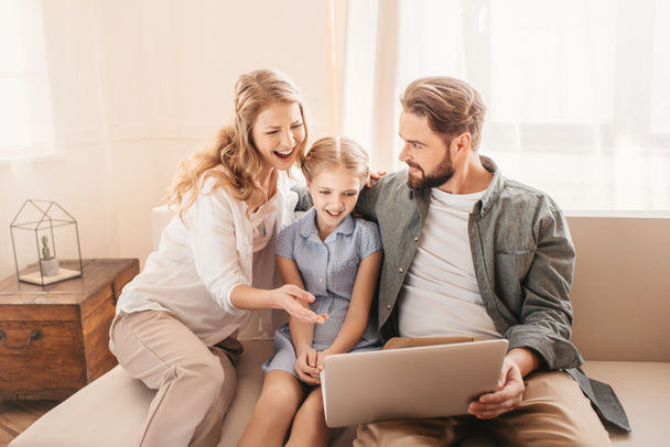 Happy family sitting on sofa and using laptop at home  - Фото, изображение