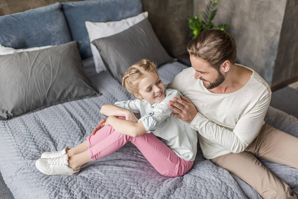 Happy adorable daughter and father sitting on bed at home  - Valokuva, kuva