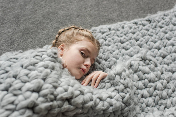 очаровательная девушка лежит на полу с серым трикотажным одеялом и смотрит в камеру
 - Фото, изображение