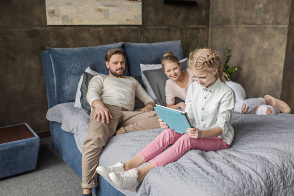 adorable daughter using digital tablet and lying on bed with parents - Valokuva, kuva