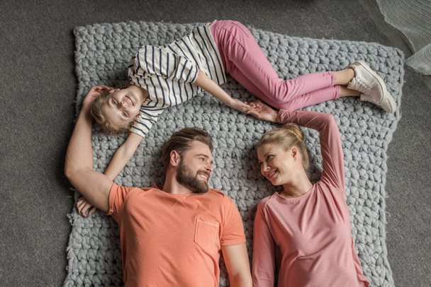 Top view of happy family with one child lying together on grey knitted carpet - Фото, зображення