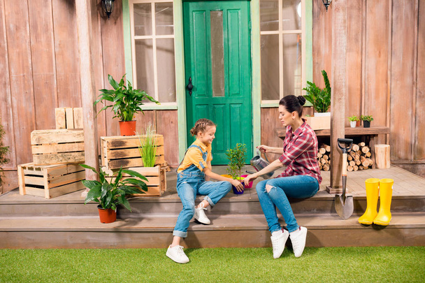 Happy mother and daughter sitting on porch and watering plant - Foto, Imagem