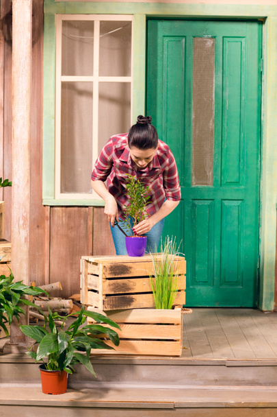 Gülümseyen genç kadın verandada duran tencerede bitki ekili  - Fotoğraf, Görsel