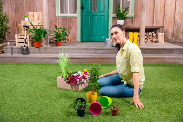 atrakcyjne ogrodnik z roślinami i doniczkami siedzi na zielonej trawie - Zdjęcie, obraz