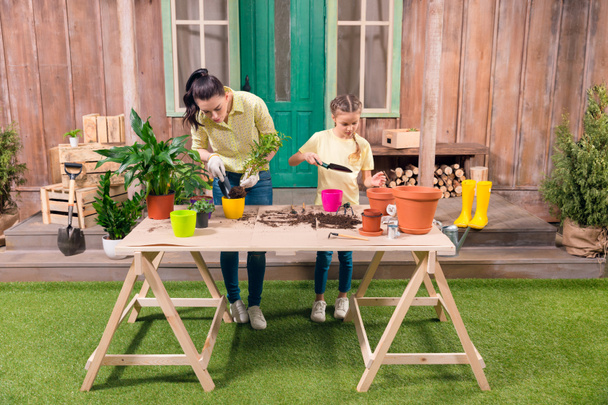 madre e hija con plantas y macetas de pie a la mesa en el porche
  - Foto, Imagen