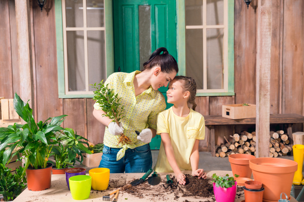 madre e hija con plantas y macetas de pie a la mesa en el porche
  - Foto, imagen