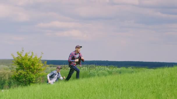 Twee tienerjongens bang na elkaar over een mooie groene heuvel tegen een blauwe hemel met wolken - Video