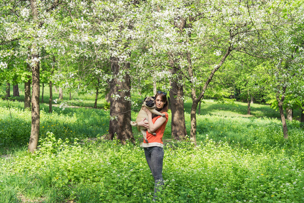 Spring. A girl with a pug dog near a burgeoning tree - Фото, изображение