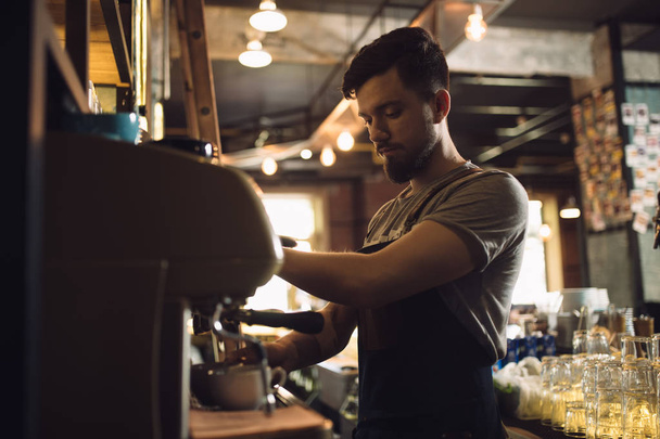Young male barista preparing drink at coffee machine - 写真・画像