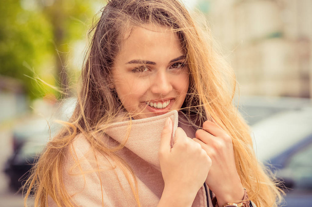 Windy. Woman happy hair on face. Closeup portrait beautiful smiling toothy sunshine girl student having cold holding collar neckband looking at you camera city background. Multicultural, mixt race. - Photo, image
