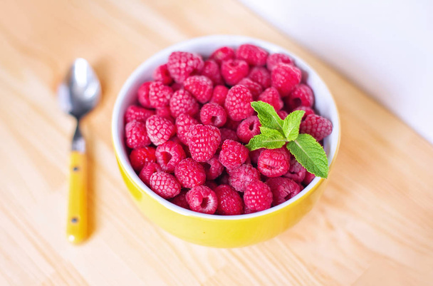Raspberries in ceramic bowl. Ripe and tasty raspberries on a wooden background. - Photo, Image