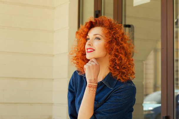 Thinking about new job new life. Beautiful red head curly woman person girl looking up thinking about future boyfriend family deciding what to do isolated outdoor street apartment complex background - Photo, image