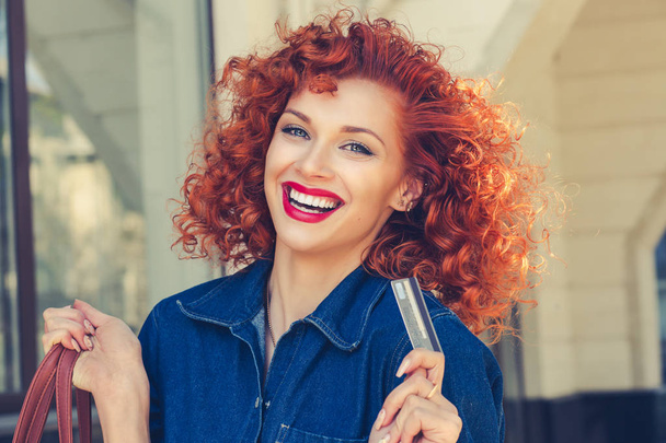 Cheerful smile woman holding showing credit card near clothing department store shopping mall outdoor Curly red head happy girl with visa at retail shop Shopaholic concept pay with credit card banking - Φωτογραφία, εικόνα