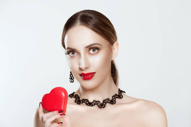Portrait on attractive, smiling young woman in beautiful necklace, holding in her hand red heart, looking at camera, isolated on white background. Positive human face expression, body language. - Foto, immagini