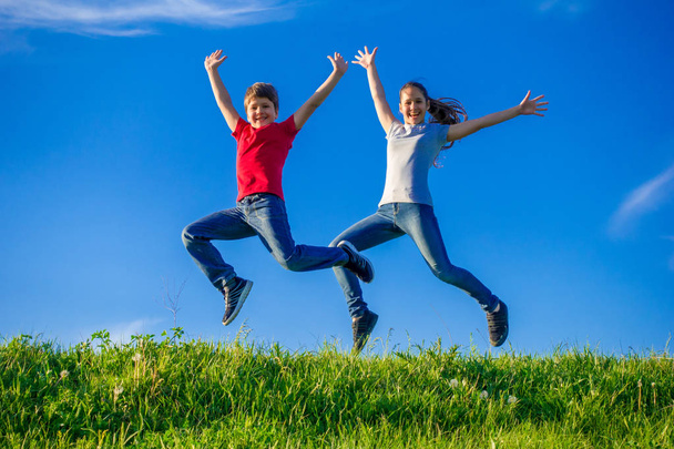Two kids jumping together on green spring hills - Foto, imagen