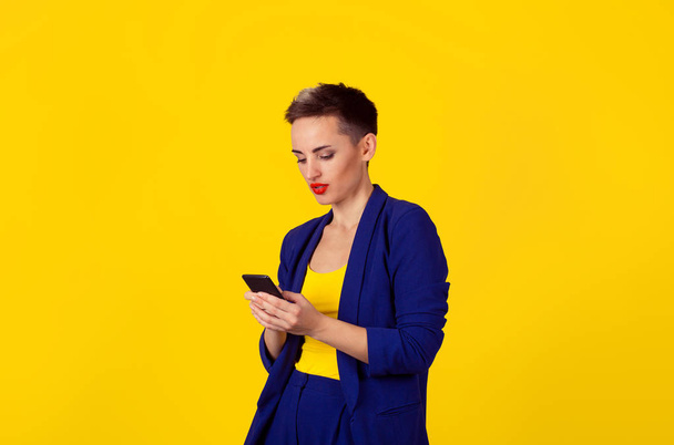Closeup portrait, serious young woman attentive excited attracted by what she sees on cell phone yellow background wall. Facial expression, reaction. Smiling girl sending text message from her mobile - Photo, image
