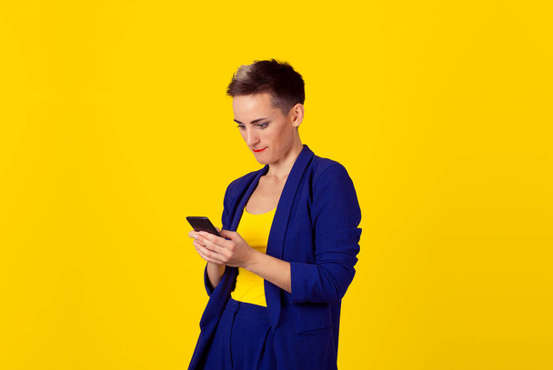 Vício em telefone. Interessado viciado mulher de negócios menina olhando para o seu telefone gadget internet isolado parede de fundo amarelo
.  - Foto, Imagem