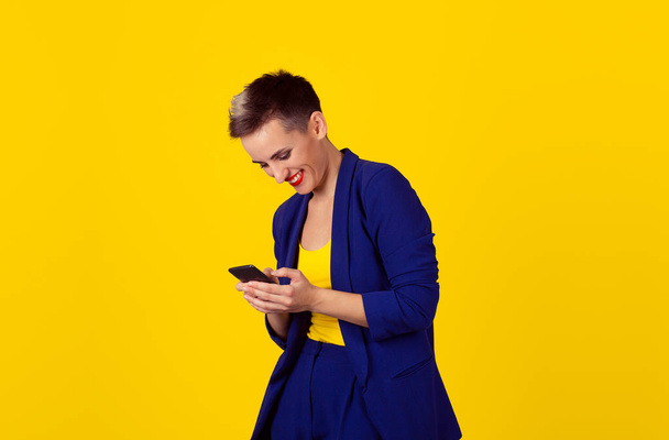 Happy chat. Closeup portrait, happy, brunette girl, smiling, looking at company cell phone, isolated yellow background. Facial expression, reaction. Business woman sending text message from her mobile - Photo, image