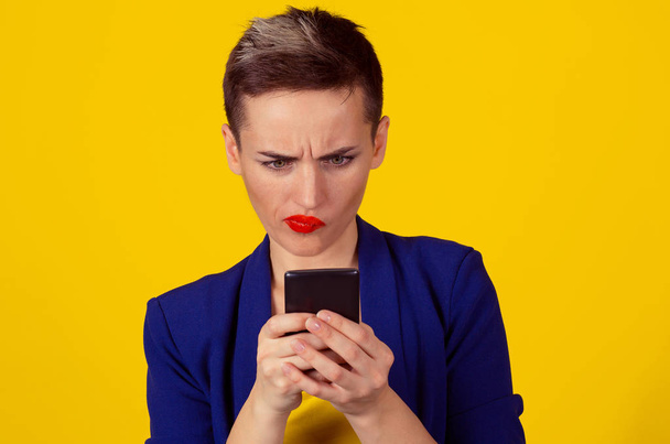 Closeup portrait upset skeptical unhappy serious woman looking at texting on phone displeased with conversation isolated on yellow background. Negative human emotion face expression feeling - 写真・画像