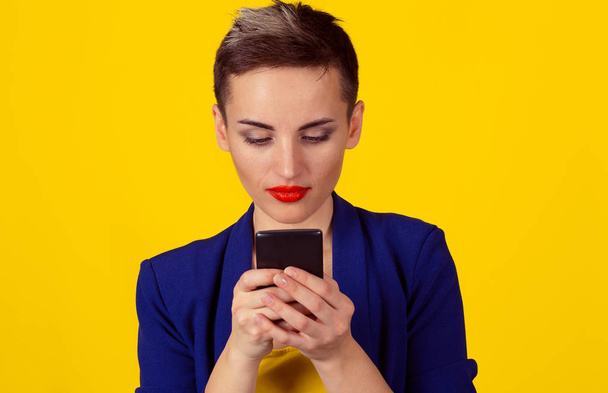 Serious business woman looking texting at phone isolated yellow background wall. Short hair, formal wear - Fotó, kép