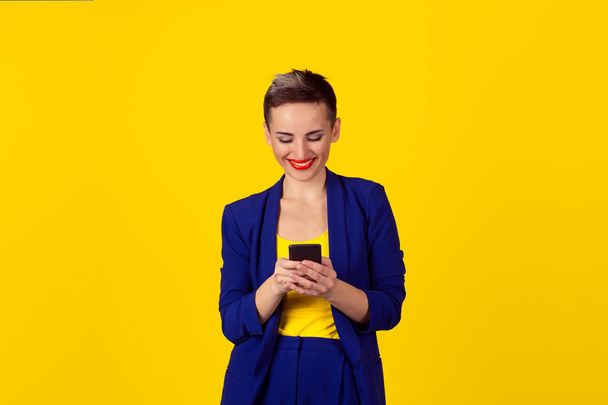 新しいスマート フォンを使用して保持している幸せな若い女性には、黄色の壁の背景に分離された世界的なインターネットの閲覧が接続されています。4 g データ計画プロバイダー - 写真・画像