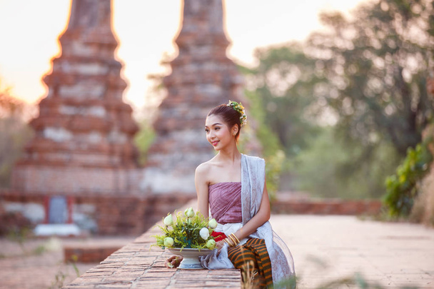 Beautiful Thai girls in thai traditional costume trying to roll up lotus flower at sunset time - Photo, image