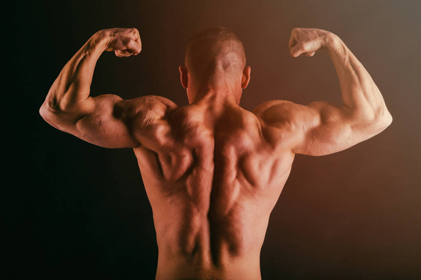 Bodybuilder posing in different poses demonstrating their muscles. Failure on a dark background. Male showing muscles straining. Beautiful muscular body athlete. - Zdjęcie, obraz