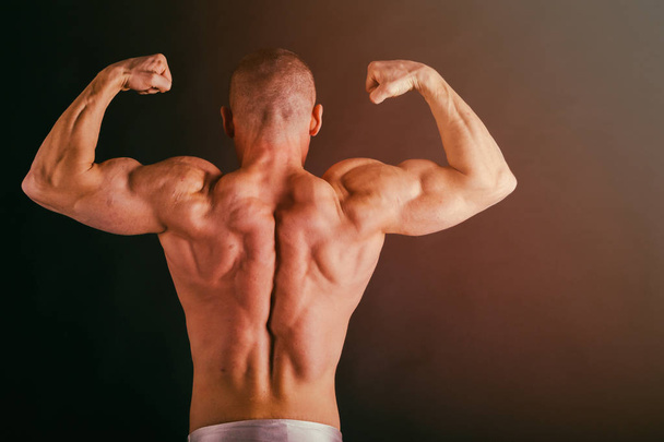 Bodybuilder posing in different poses demonstrating their muscles. Failure on a dark background. Male showing muscles straining. Beautiful muscular body athlete. - Foto, immagini