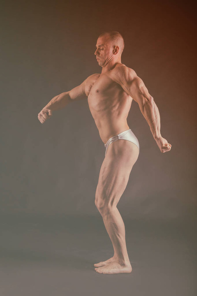 Bodybuilder posing in different poses demonstrating their muscles. Failure on a dark background. Male showing muscles straining. Beautiful muscular body athlete. - Fotoğraf, Görsel