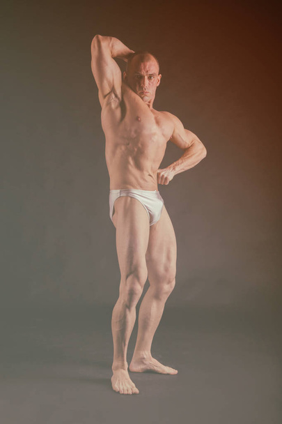 Bodybuilder που θέτουν σε διαφορετικές πόζες που αποδεικνύουν τους μυς τους. Αποτυχία σε σκούρο φόντο. Ανδρική προβολή μυς στράγγισμα. Όμορφο μυώδες σώμα αθλητής. - Φωτογραφία, εικόνα