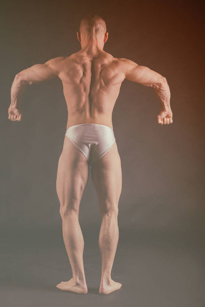 Bodybuilder posing in different poses demonstrating their muscles. Failure on a dark background. Male showing muscles straining. Beautiful muscular body athlete. - Photo, Image