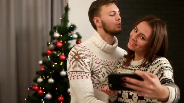 Happy young emotional couple posing on smart phone camera on christmas tree background. - Filmati, video