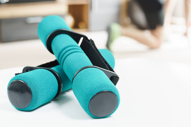 Fitness at home concept, a pair of green dumbbells in the foreground and man warming up in the background. - Fotó, kép