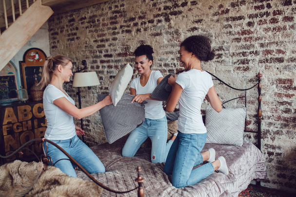 Attractive girls have fun and fight pillows on the bed. - Фото, изображение