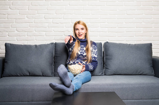 Jeune femme passe son temps libre à regarder la télévision sur le canapé à la maison, mâcher du pop-corn
. - Photo, image