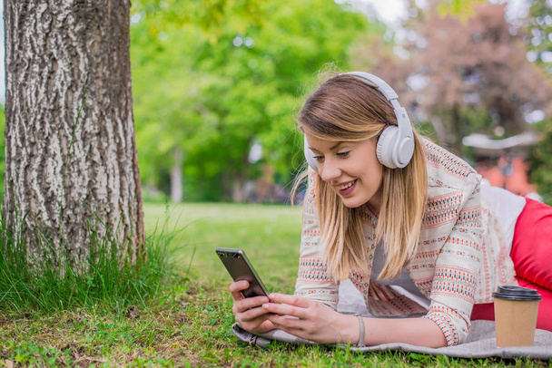 Relaxed woman listening to the music with headphones lying on the grass - Foto, immagini