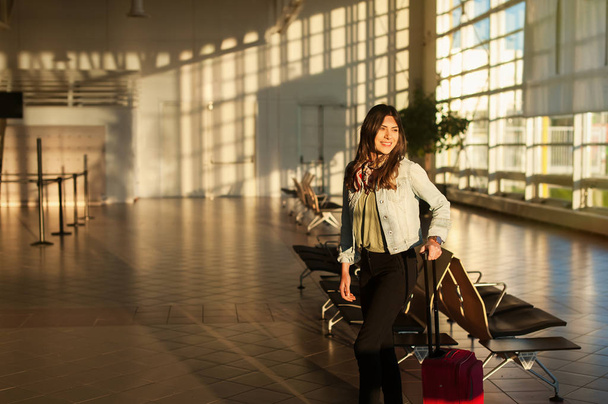 Młoda kobieta w terminalu lotniska poczekalni z torba na kółkach. - Zdjęcie, obraz
