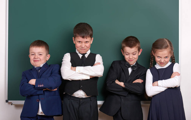 groep leerling als een bende, die zich voordeed in de buurt van leeg schoolbord achtergrond, grimassen en emoties, gekleed in klassieke zwarte pak - Foto, afbeelding