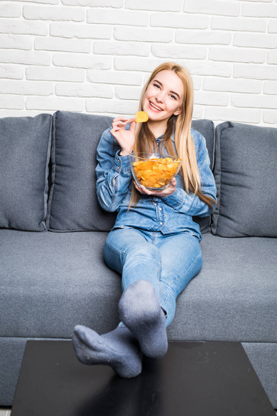 Young woman watching TV and eating chips on sofa - Foto, imagen