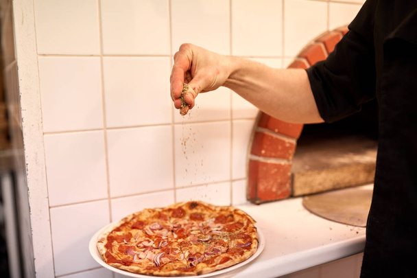cook adding pepper to salami pizza at pizzeria - Zdjęcie, obraz