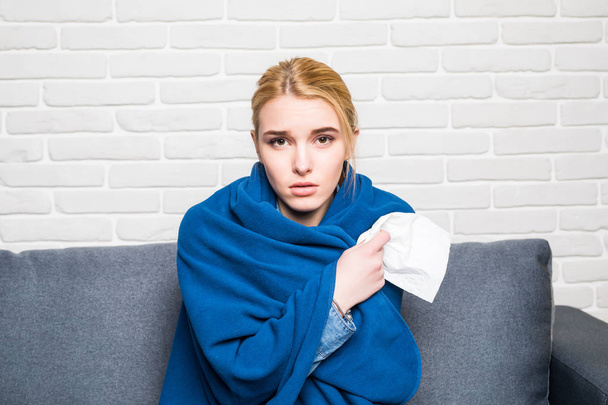 Fiatal nő érzés beteg vagy szomorú csomagolva a hangulatos kék takarót, és ül a kanapén, otthon - Fotó, kép