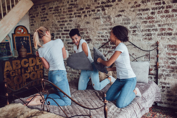 Attractive girls have fun and fight pillows on the bed. - Foto, Bild