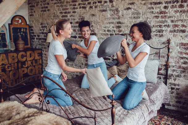 Attractive girls have fun and fight pillows on the bed. - Foto, Bild