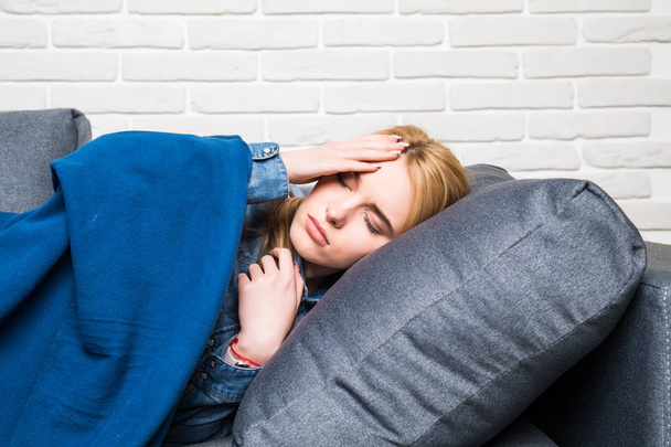 Doente jovem tira uma soneca no sofá, abraçado com um cobertor e
 - Foto, Imagem