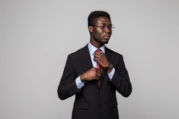 Афроамериканский бизнесмен в костюме делает галстук на сером фоне
 - Фото, изображение